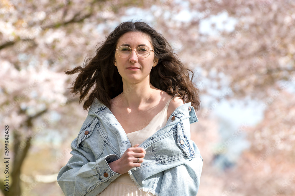 Portrait of a young tender woman against the backdrop of cherry blossoms. Dark natural hair flutters beautifully in the wind. Natural beauty of a girl. Without makeup. Portrait of a young tender woman against the backdrop of cherry blossoms. Dark natural hair flutters beautifully in the wind. Natural beauty of a girl. Without makeup.