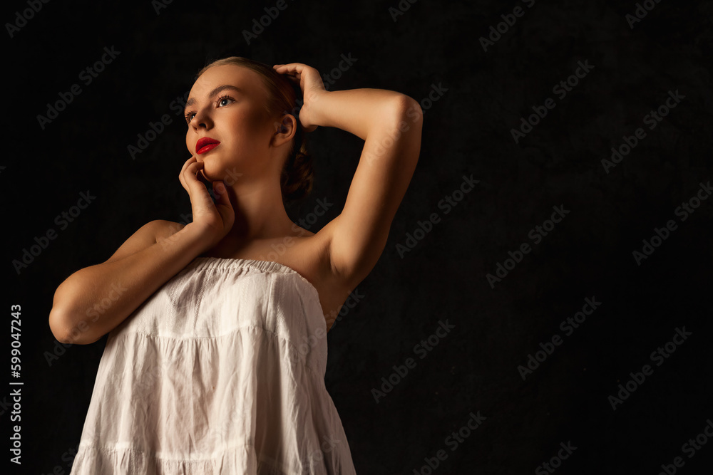 Portrait of lovely teen girl with clean skin touching face black background, thought looking away. Charming teenager with naked shoulders and perfect skin. Beauty body care concept. Copy ad text space