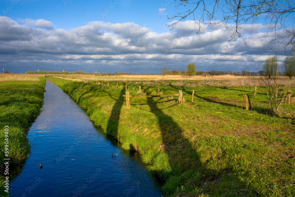 Landschaft mit einem Feld und Wassergraben und bewölktem Himmel