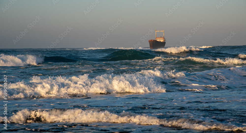Abandoned ship in the stormy sea with big wind waves at sunset. Shipwreck in the ocean