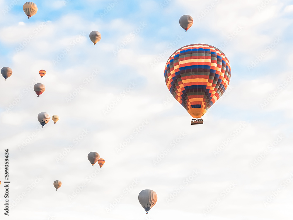 Fototapeta premium Flying in sky many bright colored beautiful balloons into air in Cappadocia in mountains early at sunrise, dawn. Filling balloon with hot air from burner, big basket. Tourists excursion, cloud flight