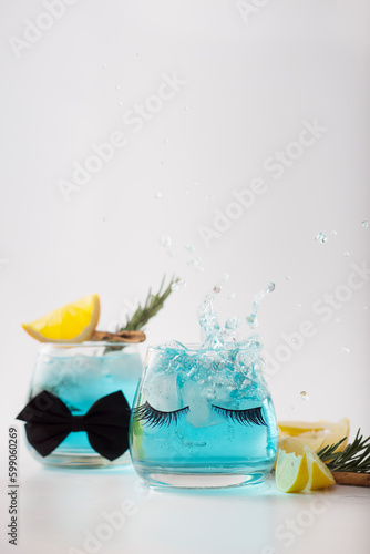 Summer cold drink closeup with drink splashing. Fresh blue cocktail with lemon, rosemary and ice in glass on white background. Studio shot in freeze motion, drops in liquid splash. Focuse on eyelashes