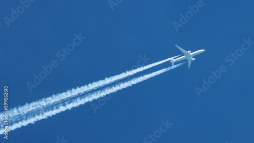 Jet airplane flying overhead in clear blue sky diagonally with condensation trail