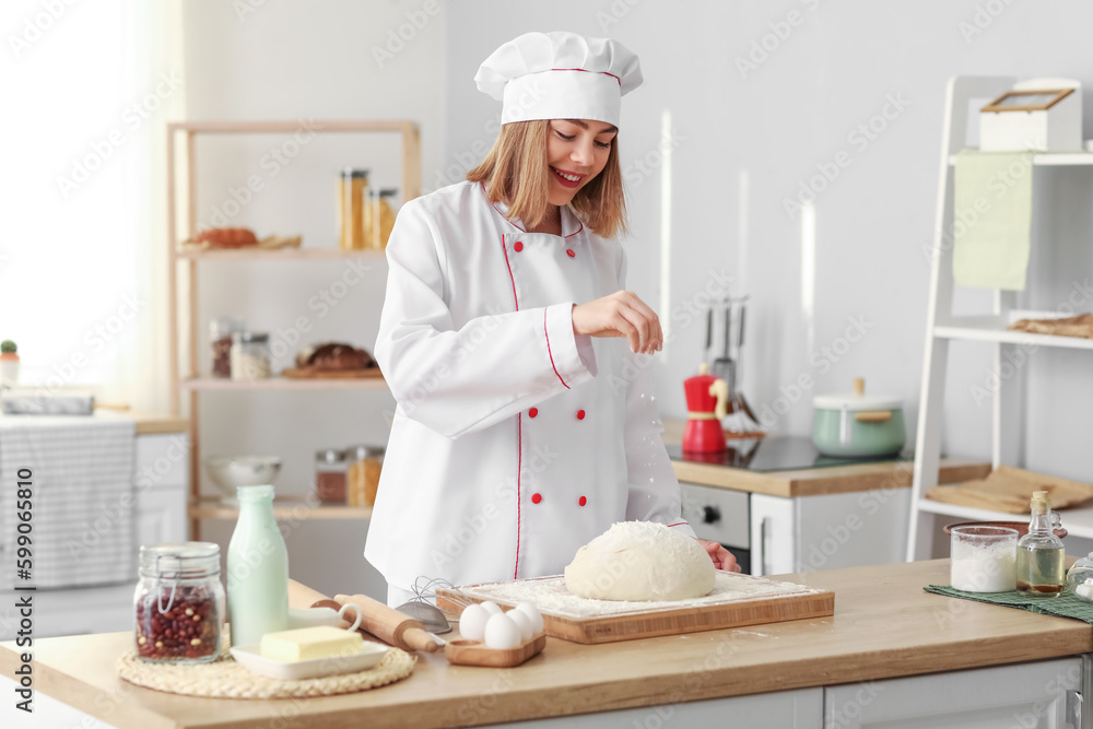 Female baker sprinkling dough with flour at table in kitchen Female baker sprinkling dough with flour at table in kitchen