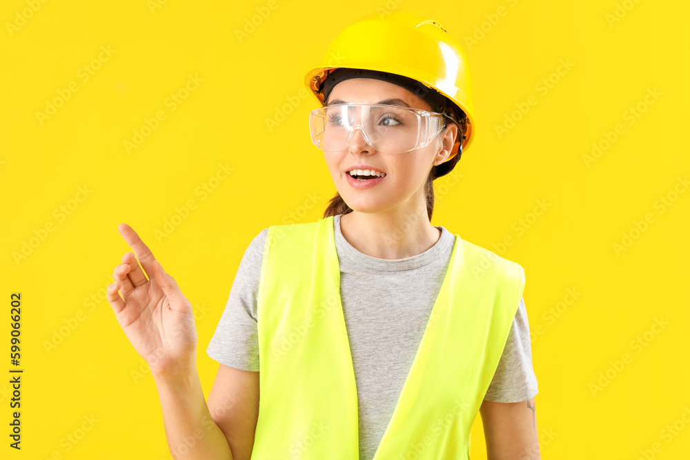 Female worker in vest pointing at something on yellow background Female worker in vest pointing at something on yellow background