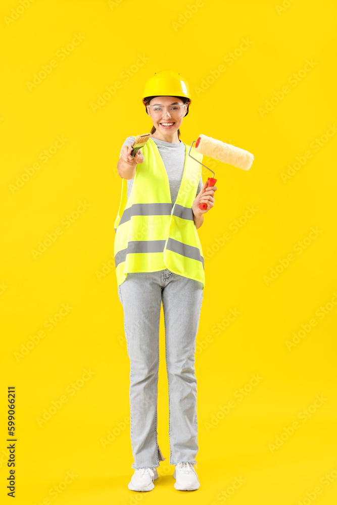 Female decorator with paint roller and brush on yellow background Female decorator with paint roller and brush on yellow background