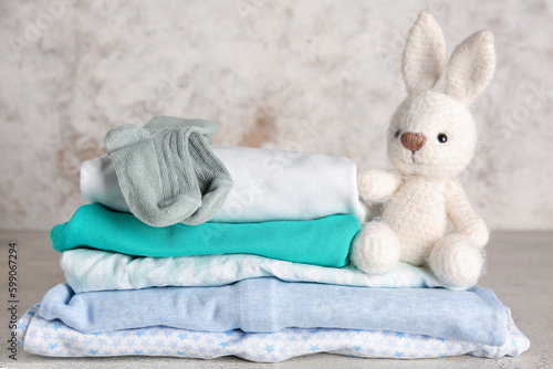 Stack of baby clothes and toy bunny on light background © Pixel-Shot