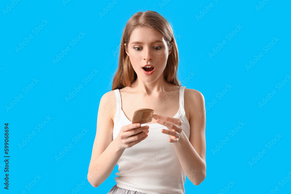 Shocked young woman with comb and fallen down hair on blue background Shocked young woman with comb and fallen down hair on blue background