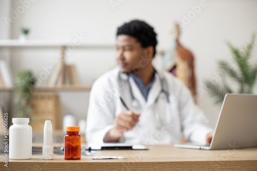 Wallpaper Mural Focus on medication containers on doctor's office desk being prescribed by medical specialist in treatment center. Busy multiethnic therapist tracking pills via laptop and writing data in document. Torontodigital.ca