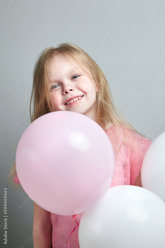 Little girl with balloon in pink knitted clothes on a gray background. Portrait of cute smiling girl, happy childhood Little girl with balloon in pink knitted clothes on a gray background. Portrait of cute smiling girl, happy childhood