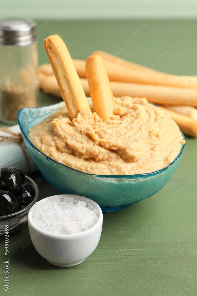 Bowl with tasty hummus and Italian Grissini on green wooden background Bowl with tasty hummus and Italian Grissini on green wooden background