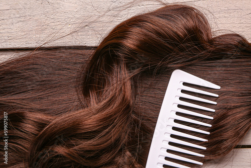 Curled brown hair with comb on grey wooden background, closeup