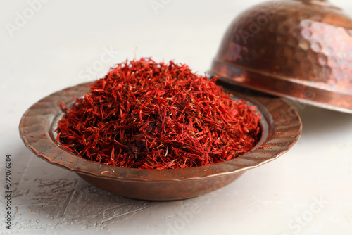 Bowl with pile of saffron on light background
