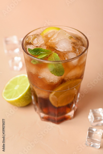 Glass of cold Cuba Libre cocktail on beige background