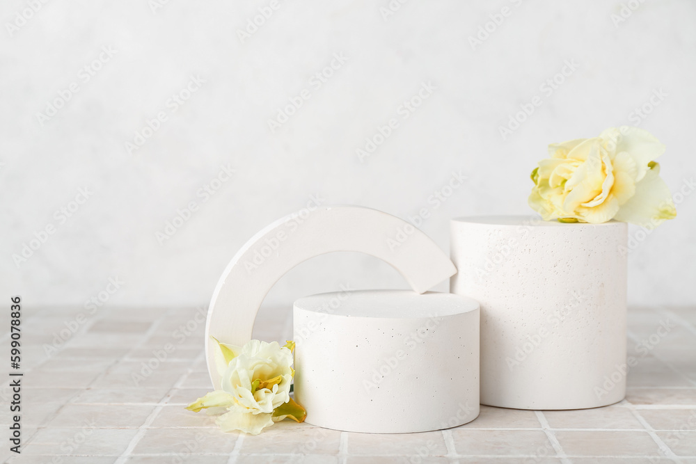 Decorative plaster podiums with daffodils on grey tile against white wall