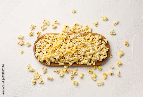 Wooden board with crispy popcorn on light background