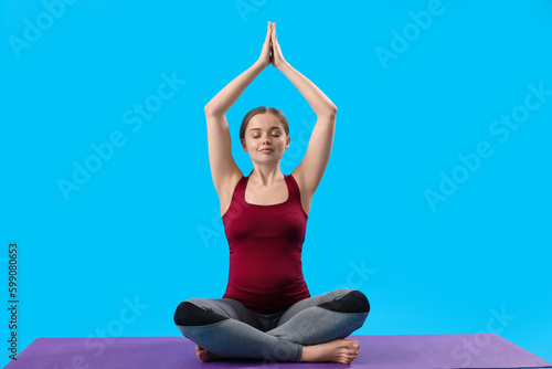 Pregnant young woman doing yoga on blue background