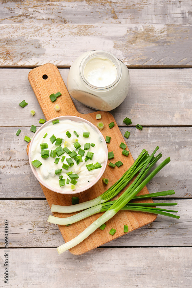 Bowl and jar of tasty sour cream with green onion on light wooden background Bowl and jar of tasty sour cream with green onion on light wooden background