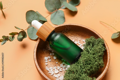 Wooden plate with bottles of cosmetic oil and eucalyptus branch on orange background