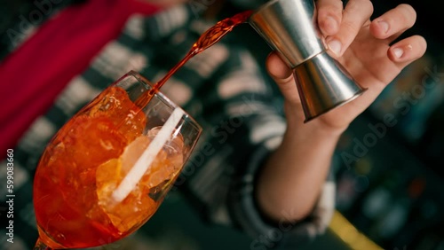 Preparation of Aperol Spritz cocktail bartender pouring prosecco into a glass with ice at the bar close-up