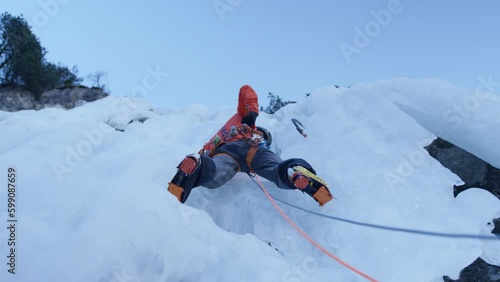 An athlete climbs an icefall with ice axes and crampons in the Alps, Switzerland
