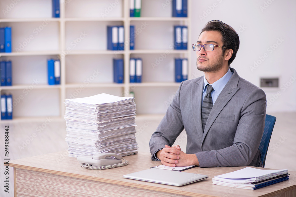 Young male employee and too much work at workplace Young male employee and too much work at workplace