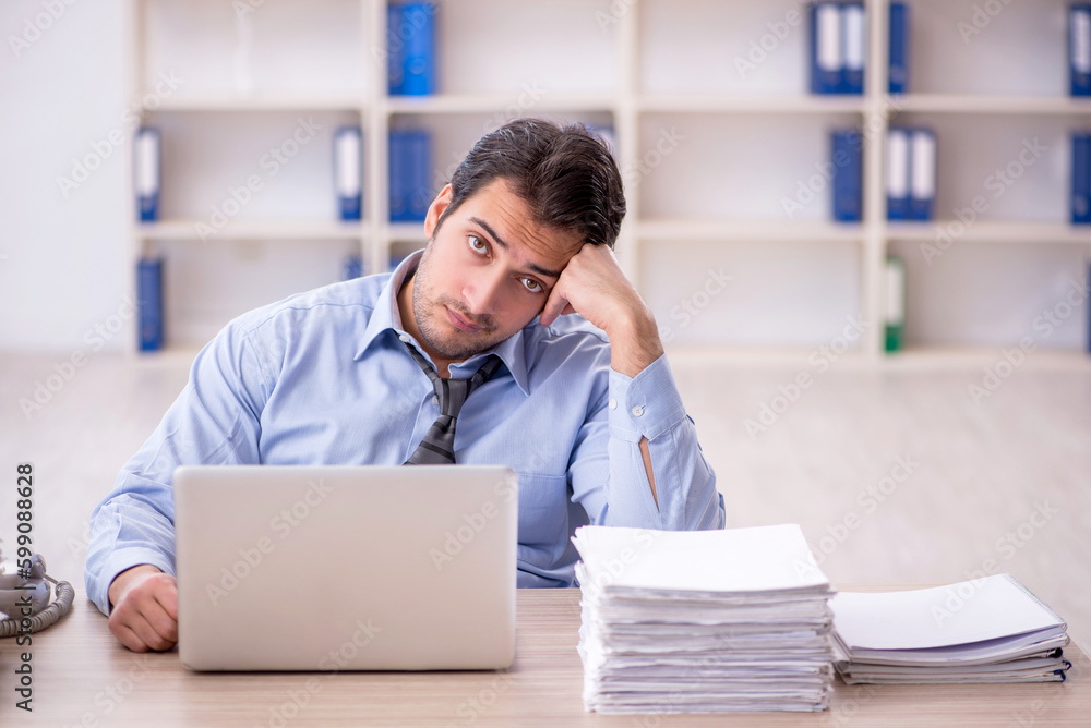 Fototapeta premium Young male employee and too much work at workplace