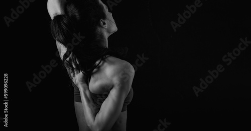 Sporty healthy body woman with strong muscular shoulders and blades doing hands in the lock exercise behind the back on black shadow background. Closeup studio