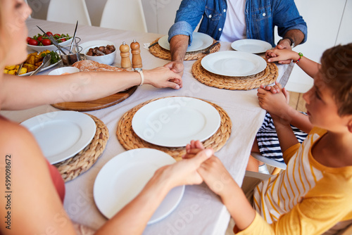 Give thanks for the simple things. a family holding hands in prayer before having a meal together.