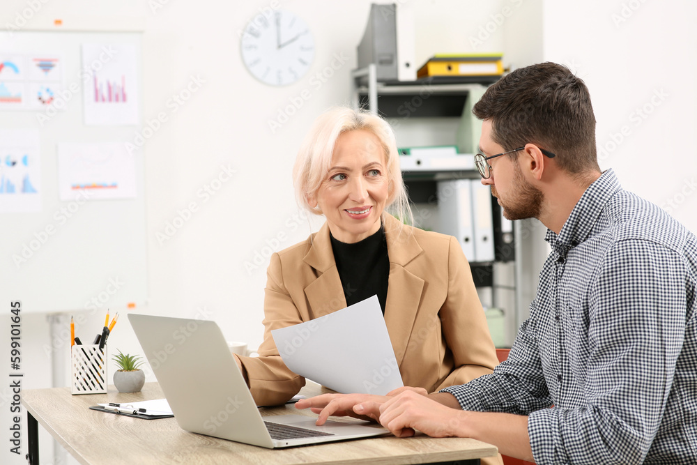 Boss and employee with laptop discussing work issues at wooden table in office Boss and employee with laptop discussing work issues at wooden table in office