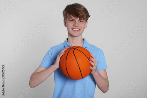Teenage boy with basketball ball on light grey background © New Africa