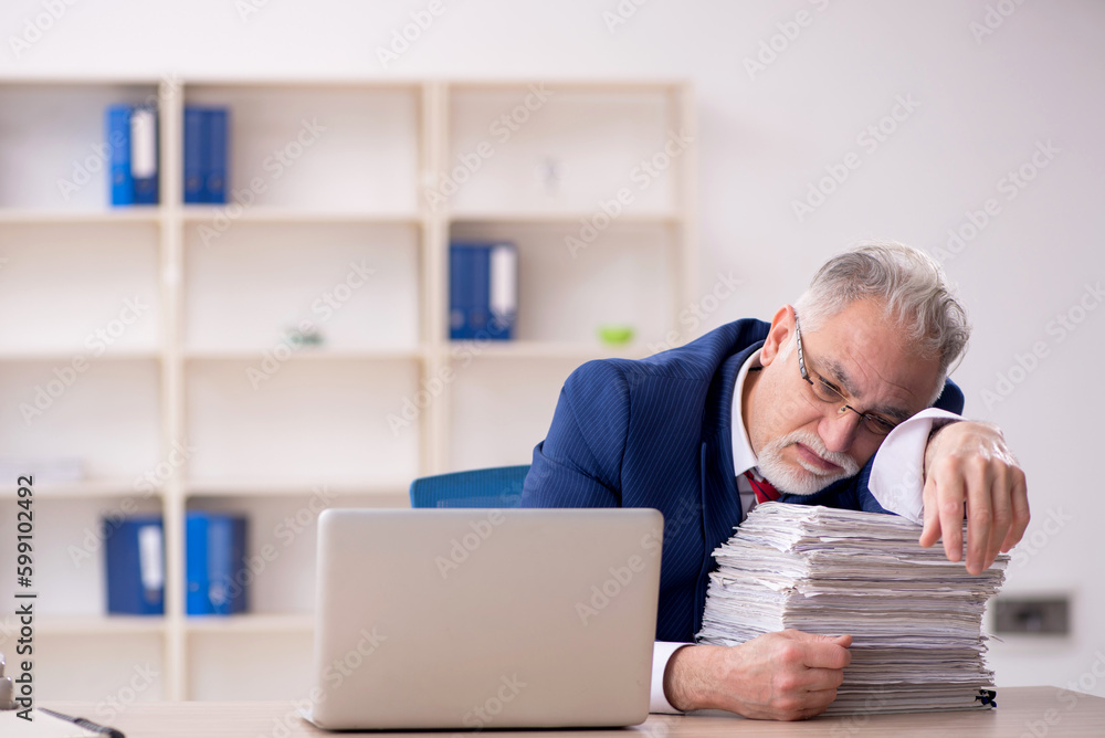 Old male employee unhappy with excessive work in the office Old male employee unhappy with excessive work in the office