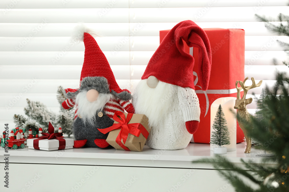 Fototapeta premium Funny Christmas gnomes and gift boxes on commode in room with festive decoration
