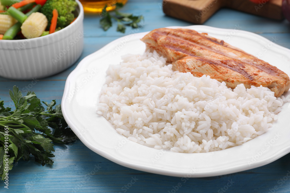 Grilled chicken breast and rice served with vegetables on light blue wooden table, closeup