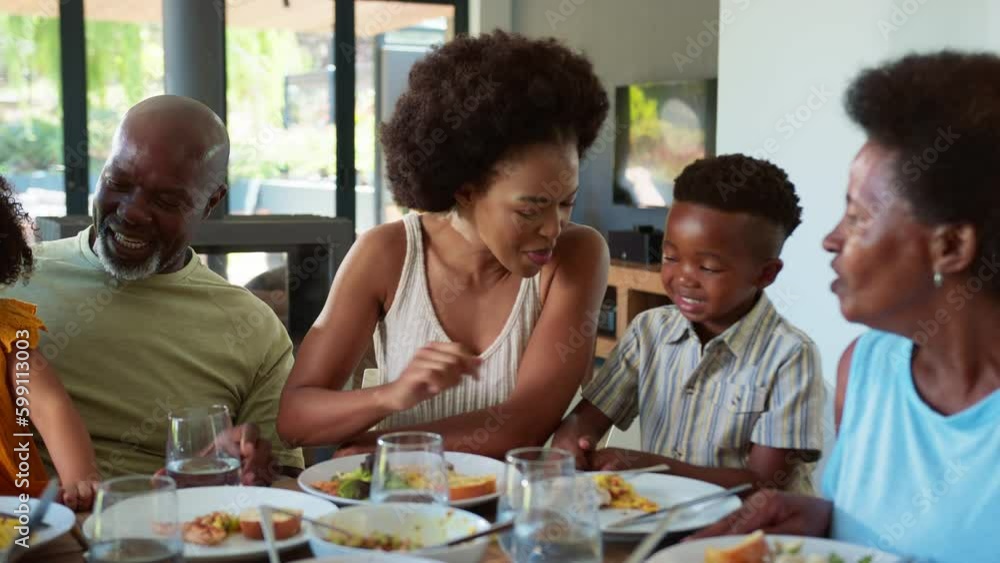 Smiling multi-generation family sitting around table at home eating meal together-shot in slow motion Smiling multi-generation family sitting around table at home eating meal together-shot in slow motion