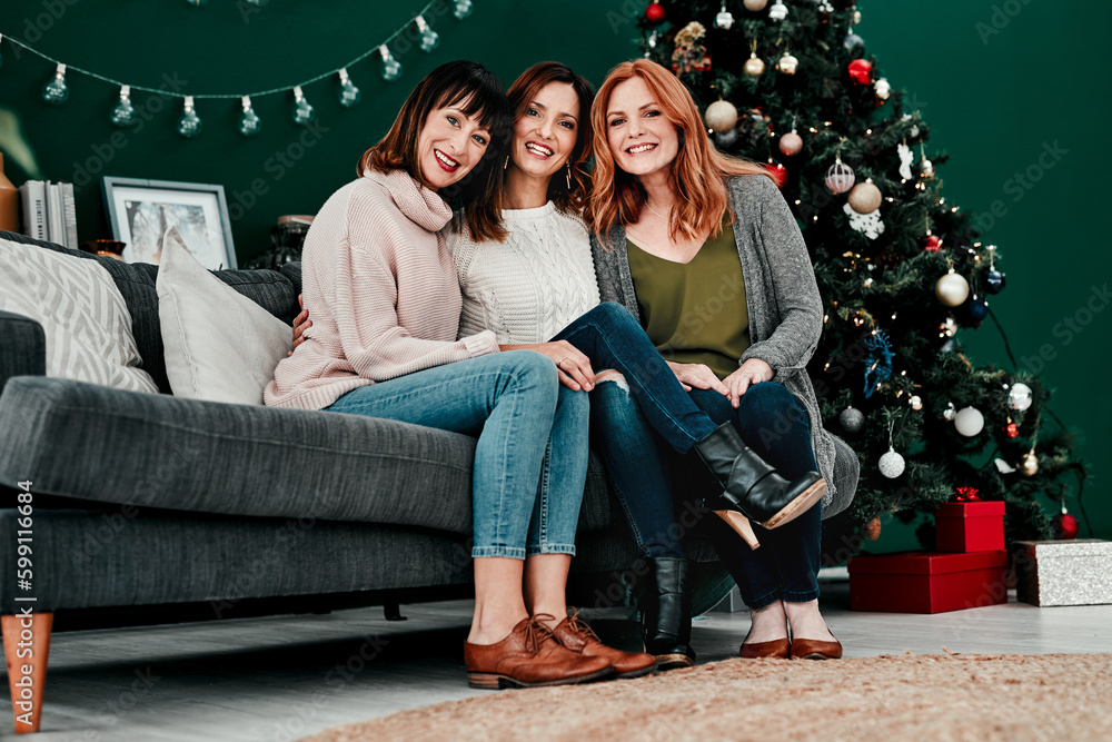 Best friends forever. Portrait of three attractive middle aged women seated together on a sofa with a Christmas tree in the background at home.