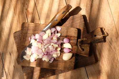Sliced onion and garlic on a wooden cutting board. stainless steel knife for slicing. served on a rustic brown wooden table. Onion and garlic are spices for cooking. bawang merah, bawang putih iris. photo