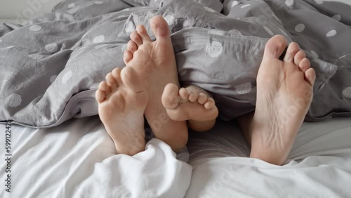 Closeup of a couple's feet playing footsie under a fluffy blanket on a cozy bed. The footage represents the playful, loving relationship of a couple and the joys of being at home together photo