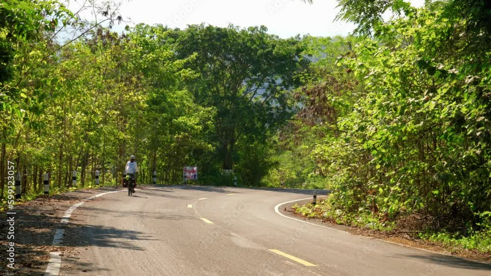 A lone female cyclist coasts down a road near Paknai's Fisherman Village in the Na Muen District, Nan, Thailand. Handheld static footage A lone female cyclist coasts down a road near Paknai's Fisherman Village in the Na Muen District, Nan, Thailand. Handheld static footage