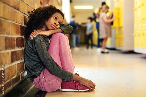 School really isnt for me. Full length shot of a young girl sitting in the hallway at school and feeling depressed. photo