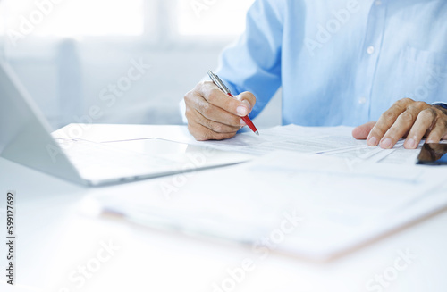 Asian businessman reviewing document reports at office workplace with computer laptop. legal expert; professional lawyer reading and checking financial documents or insurance contract