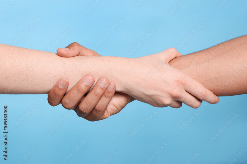 International relationships. People holding hands on light blue background, closeup International relationships. People holding hands on light blue background, closeup