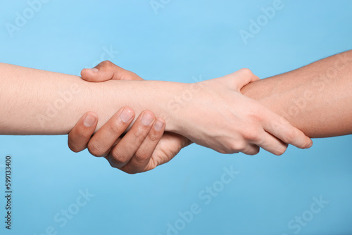 International relationships. People holding hands on light blue background, closeup