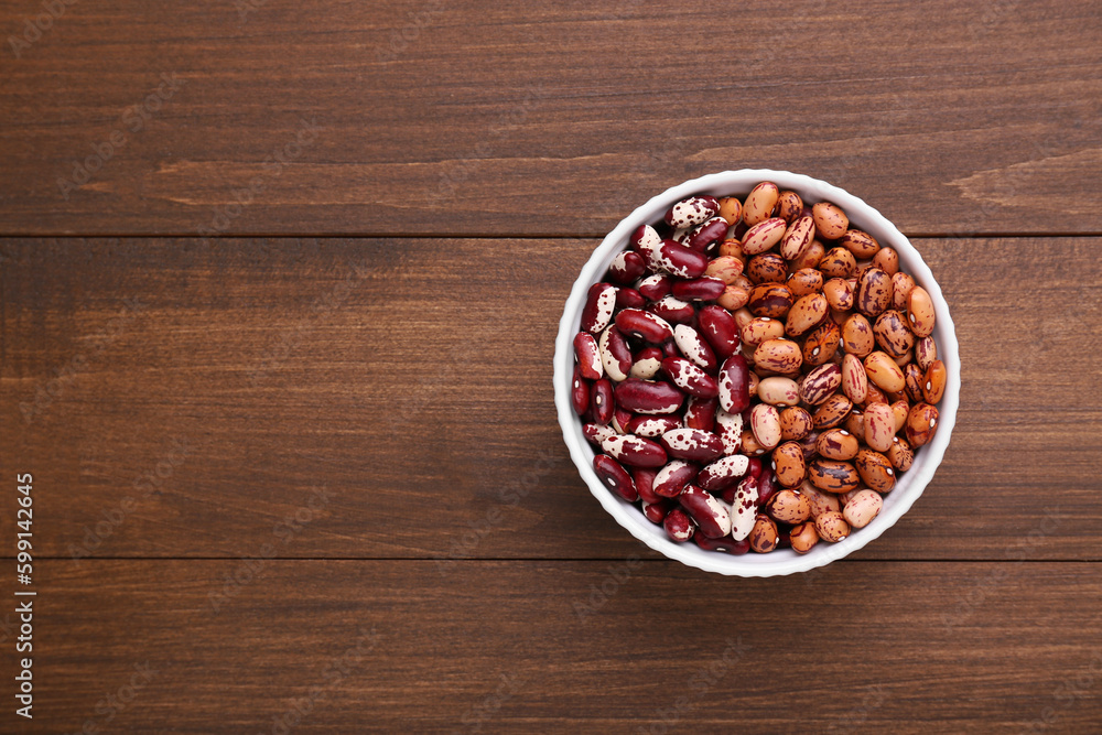 Different kinds of dry kidney beans in bowl on wooden table, top view. Space for text Different kinds of dry kidney beans in bowl on wooden table, top view. Space for text