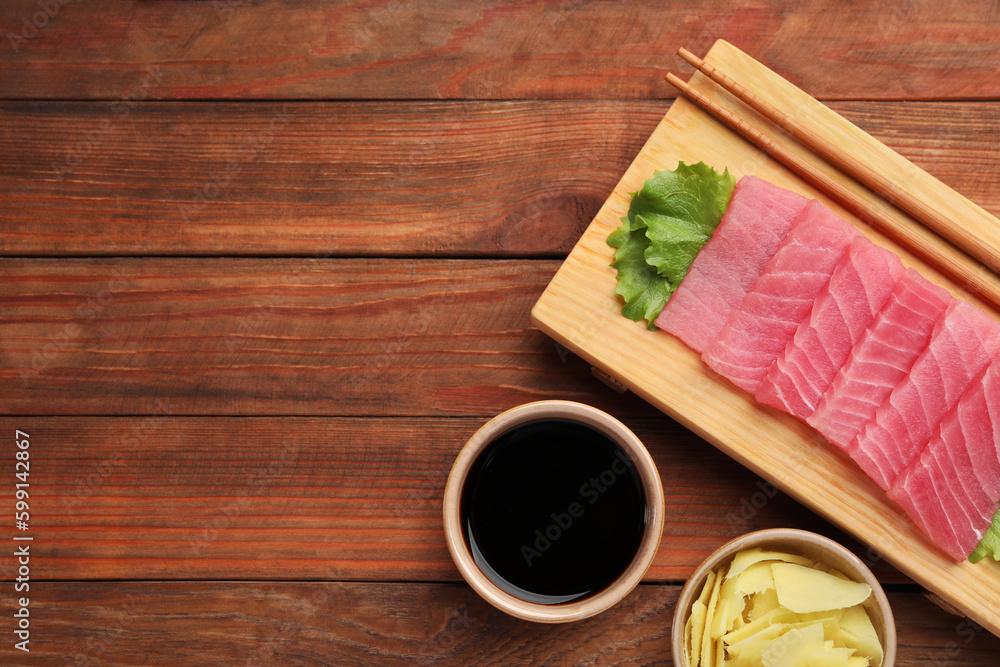 Tasty sashimi (pieces of fresh raw tuna), lettuce, soy sauce and ginger slices on wooden table, flat lay. Space for text