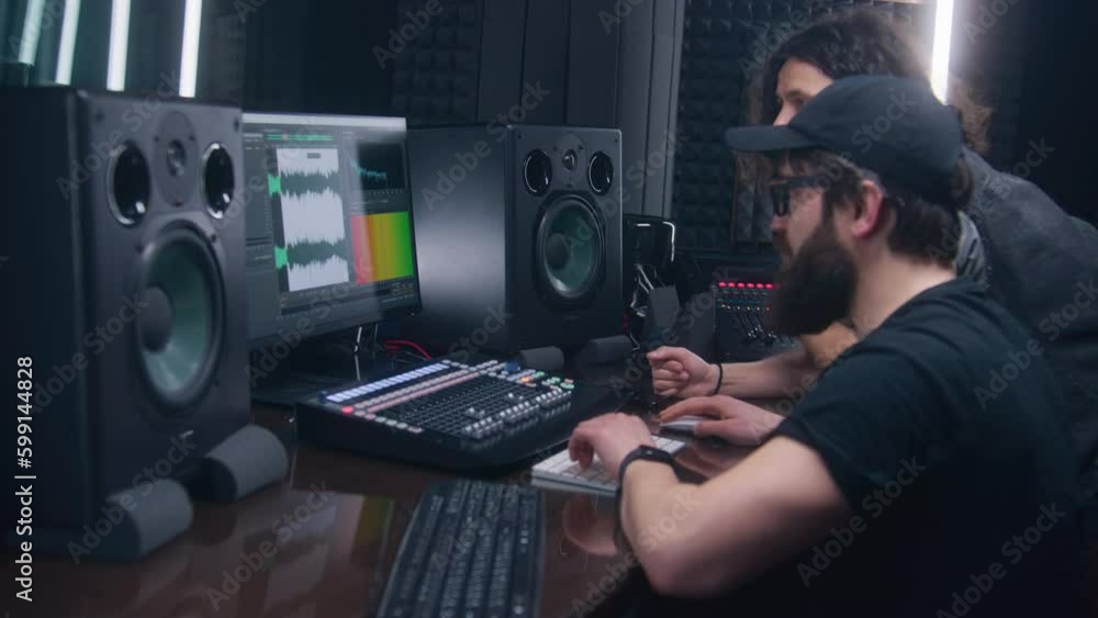 Sound engineer and musician create song in music recording room. Computer screen showing DAW software interface with sound track. Modern equipment in sound recording studio. Music production concept.