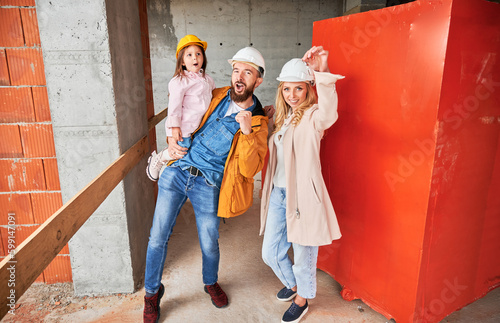 Man holding daughter and smiling. Happy couple real estate house buyers demonstrating keys from new home under construction. Family life and new home purchase concept. © anatoliy_gleb