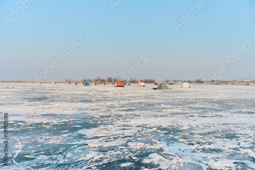 Winter landscape on a frozen lake, people and tents, winter fish