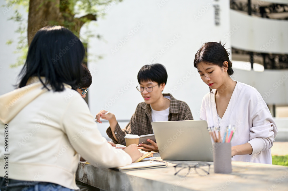 Focused Asian female college student working on a school project with her friends Focused Asian female college student working on a school project with her friends