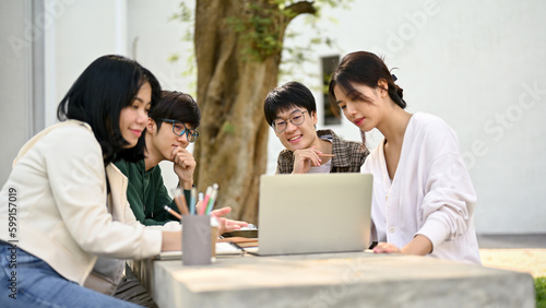 Group of happy Asian college students looking at a laptop screen, discussing their school project
